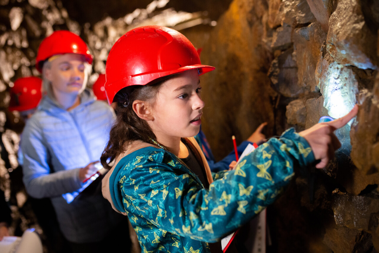 Dziewczynka w czerwonym kasku dotyka skał w podziemiach Kopalni Srebra
