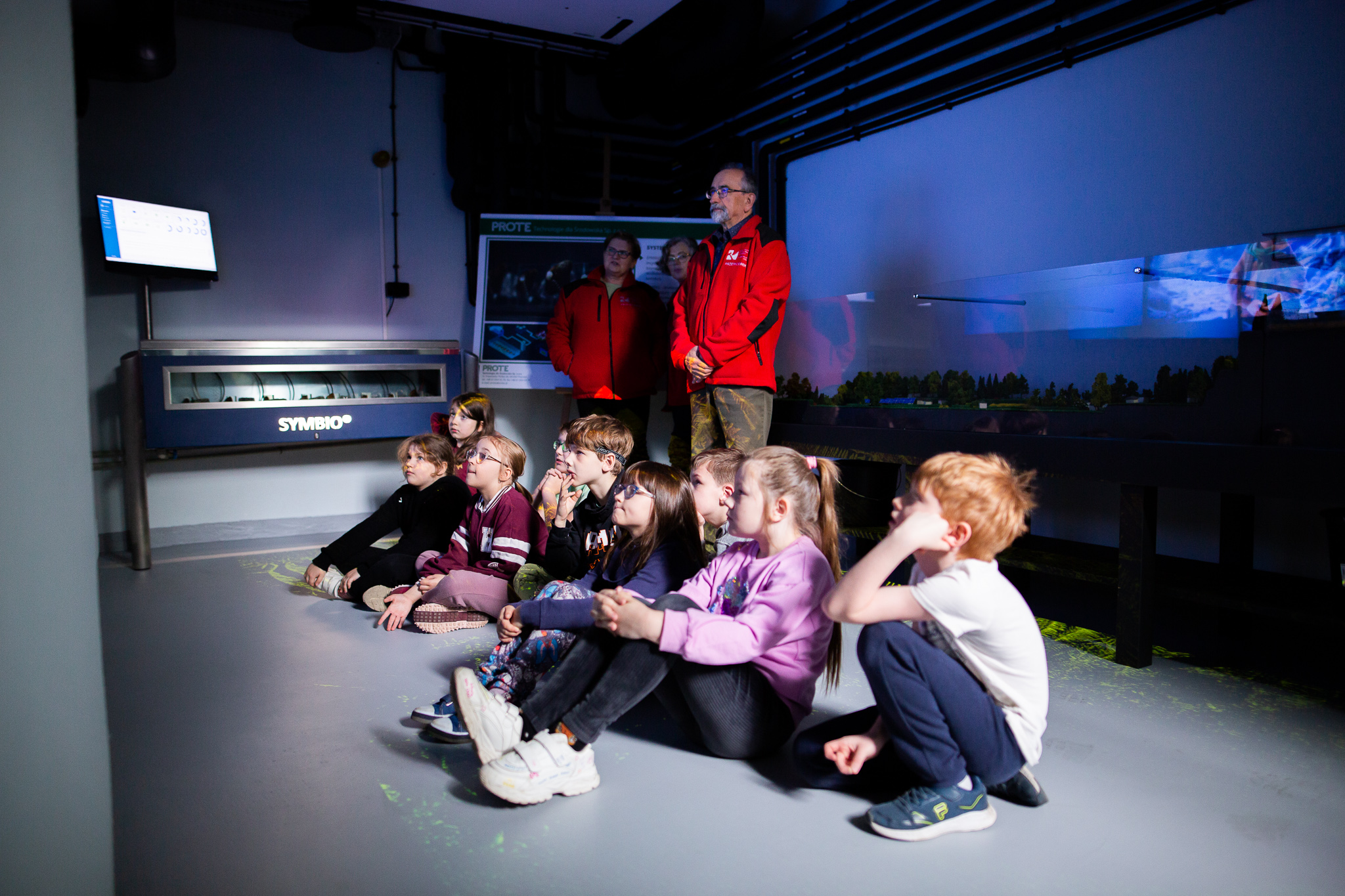 Dzieci szkół podstawowych podczas lekcji z edukatorem - oglądający film.