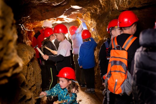 Grupa dzieci stukająca kilofkami w skały podczas lekcji edukacyjnej w podziemiach Zabytkowej Kopalni Srebra