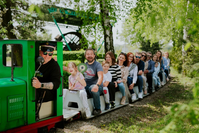 Uśmiechnięci ludzie siedzący na małej kolejce skansenowej